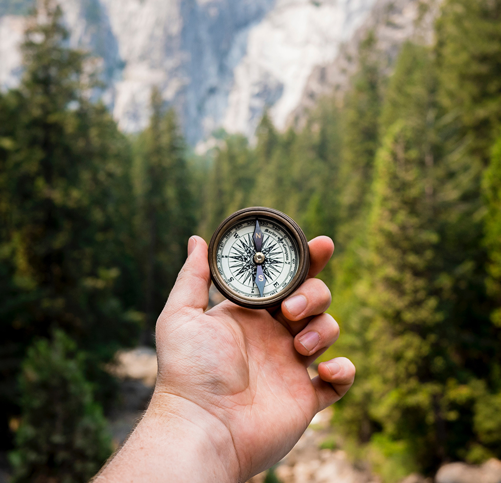 hand holding compass against mountainous background